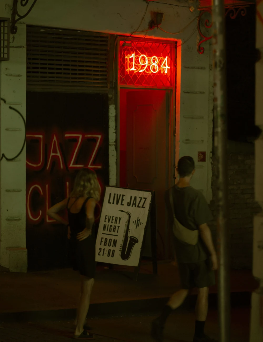 Guests arrive at a live jazz club beneath red neon and a sign announcing music every night.