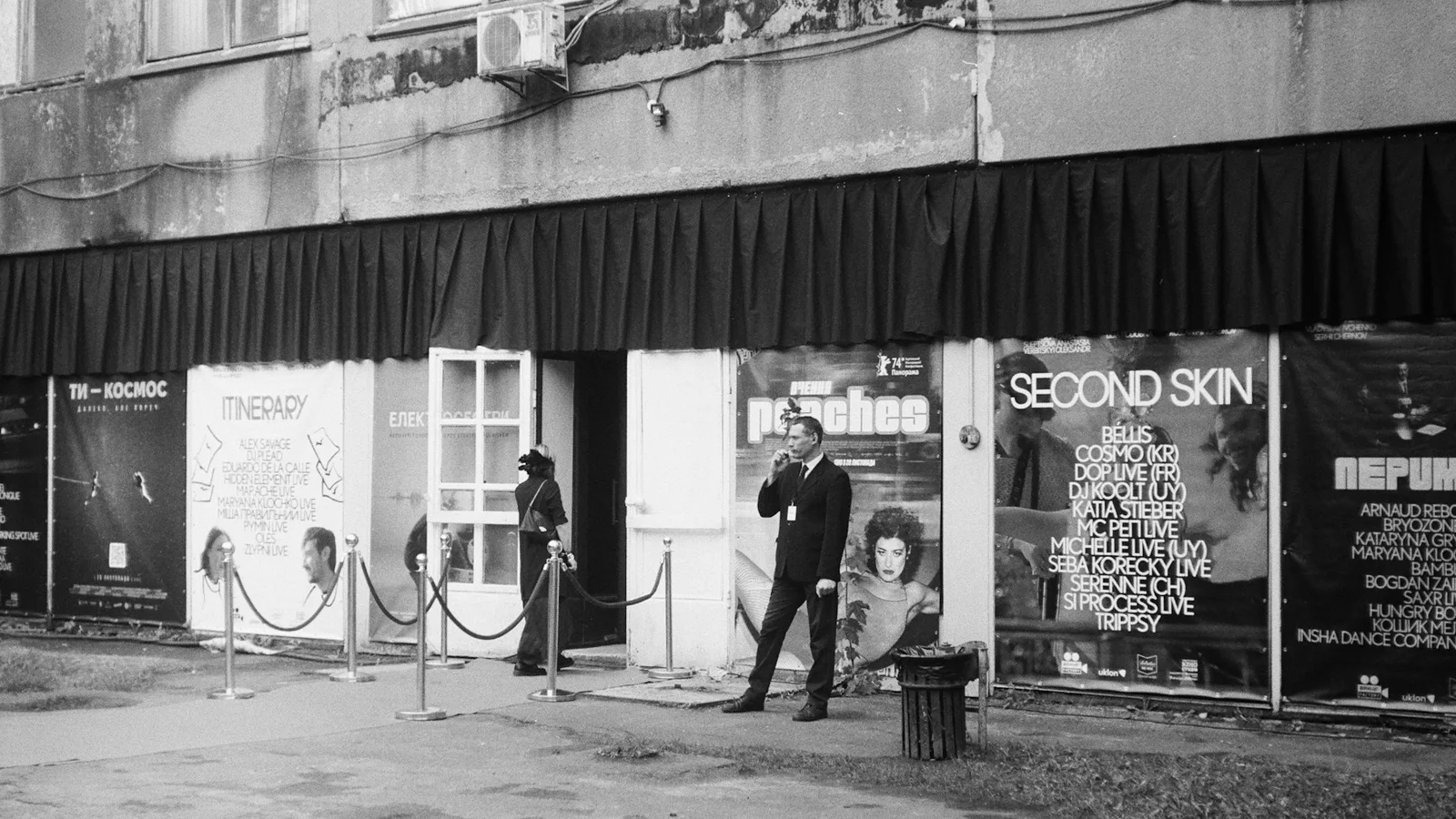 A venue door host stands beside the entrance ropes outside an independent club.