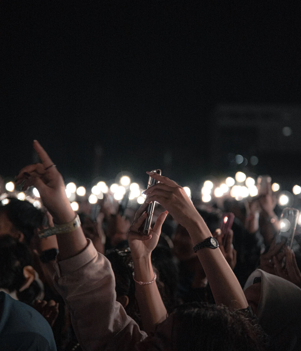 Concertgoers hold up phones and lights during a live performance at night.